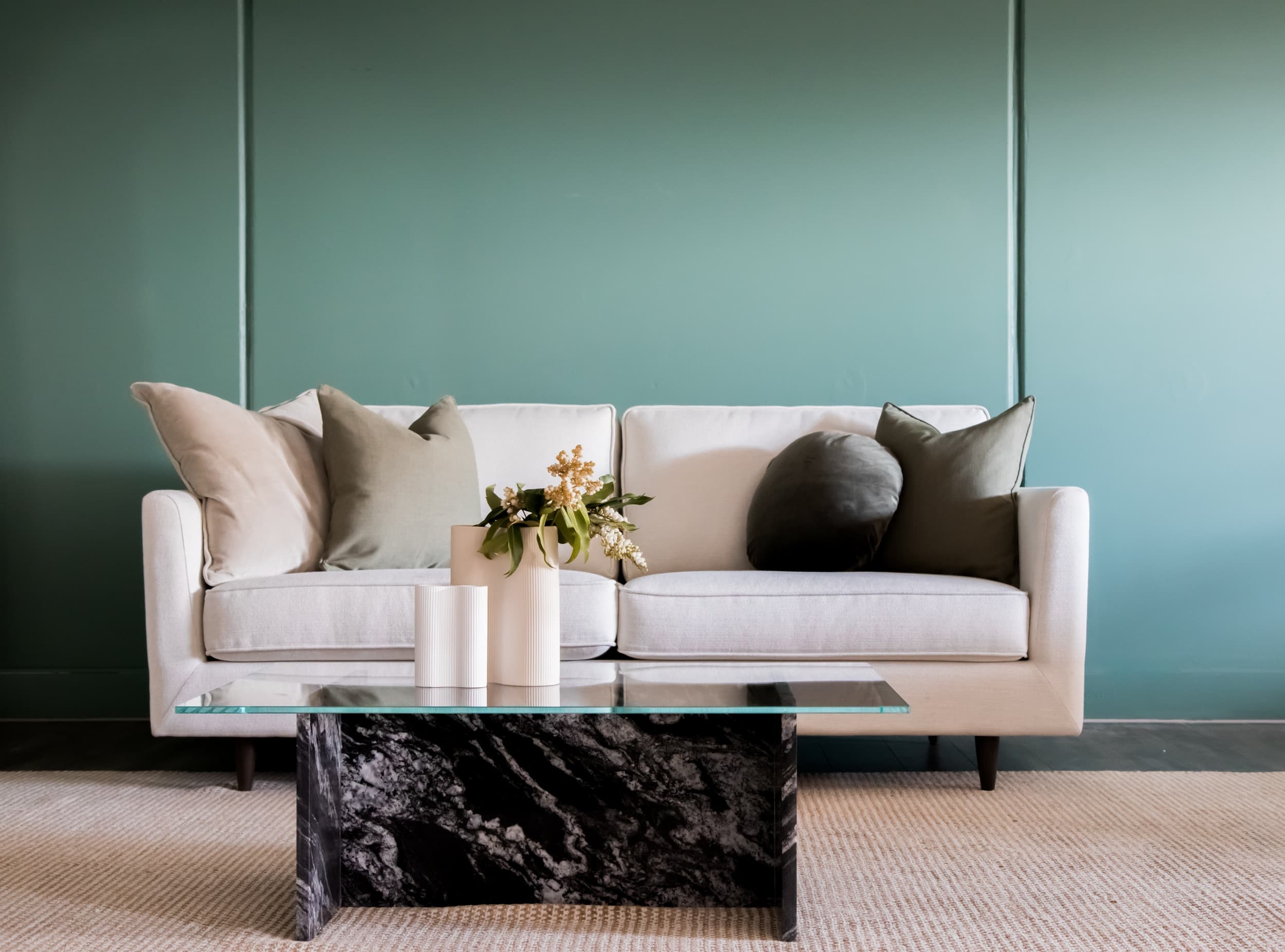 A pale sofa and glass coffee table against a green wall